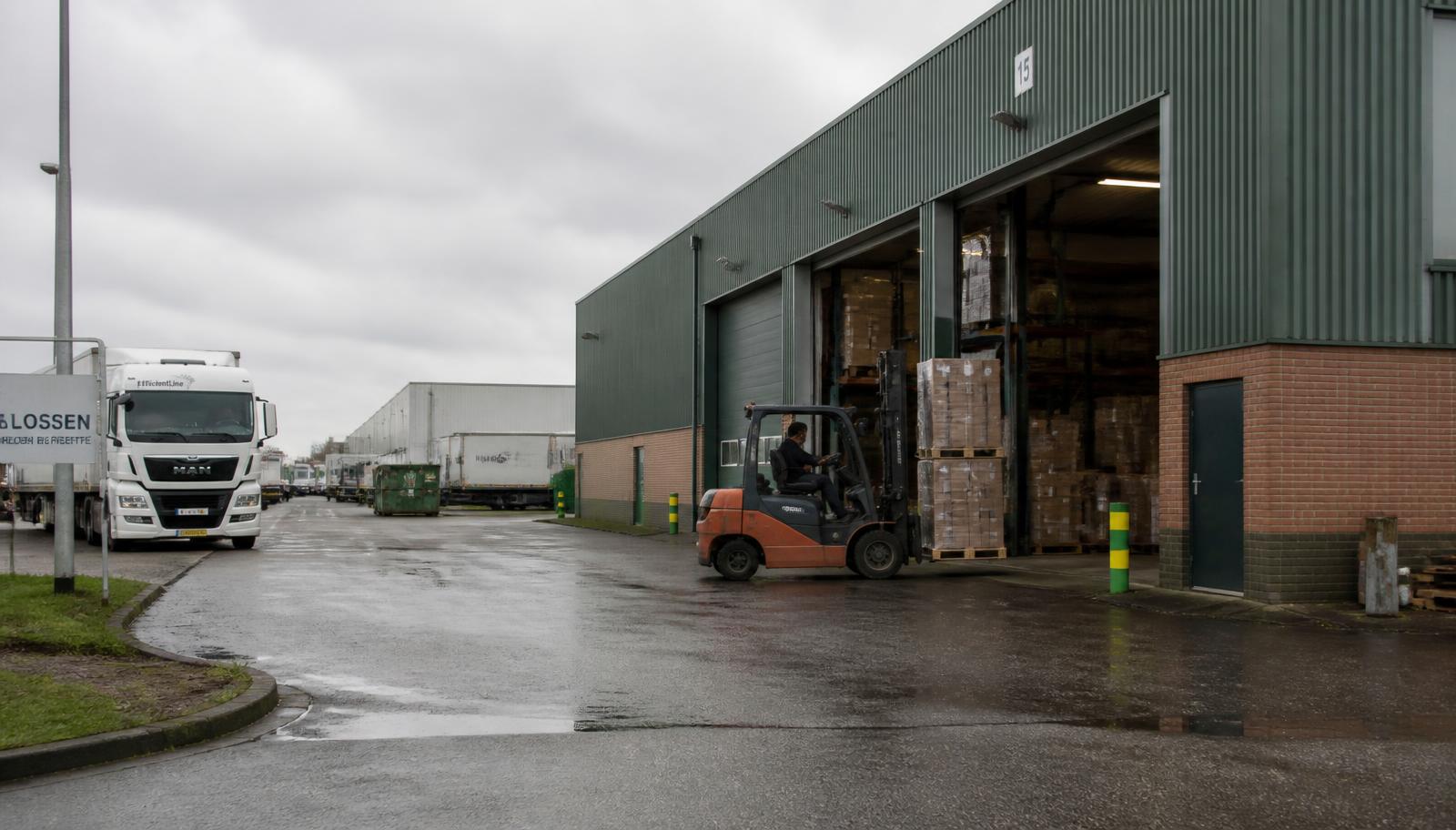 Branchecijfers — betaaltermijnen en faillissementsdichtheid per bedrijfstak Nederlands bedrijventerrein met distributiecentrum, geparkeerde vrachtwagens en een heftruck bij het laaddok